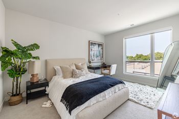 A bedroom with a large bed and a view of the outdoors through a large window.